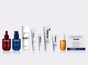 A lineup of REMEDY skincare products on a light gray background, including a red dropper bottle, a blue pump bottle, several white tubes and bottles, and a box of CLEAN TOWELS Original.